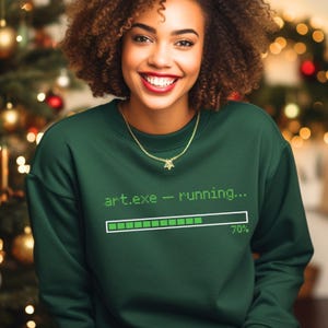May include: A dark green sweatshirt with the text "art.exe - running..." and a progress bar at 70%. The person is wearing a gold necklace with a star pendant. The background is blurred with Christmas lights.
