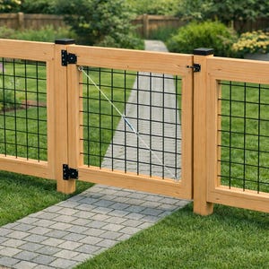 May include: A wooden garden fence with a gate, incorporating black wire mesh. The gate is ajar, showing a stone path leading into a garden. The fence is constructed from light-coloured wood and has black metal hinges.