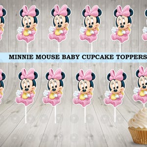 May include: Ten pink and white Minnie Mouse baby cupcake toppers. Each topper features a cartoon image of Minnie Mouse wearing a pink dress and a bow. The text "MINNIE MOUSE BABY CUPCAKE TOPPERS" is printed in white on a blue banner.