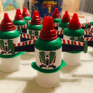Op de afbeelding: Groene en rode feestflesjes met een wit etiket waarop een cartoon-trein staat met de tekst "Jayden Party 1".