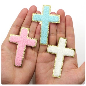 May include: Three felt cross shapes with gold glitter trim. The crosses are pink, light blue, and white.