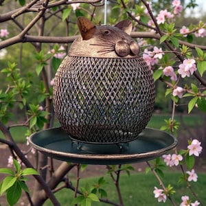 Peut inclure: Mangeoire à oiseaux décorative en forme de chat, en métal bronze. Le corps est en treillis métallique. Elle est suspendue à une branche d'arbre, avec un plateau en dessous, entourée de fleurs roses, pour le jardin.
