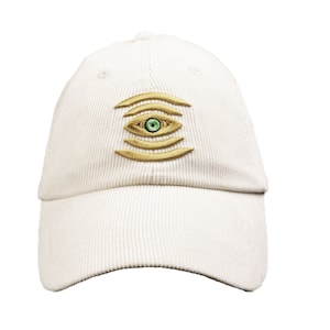 May include: A white corduroy baseball cap with a gold embroidered eye design. The eye has a green iris.