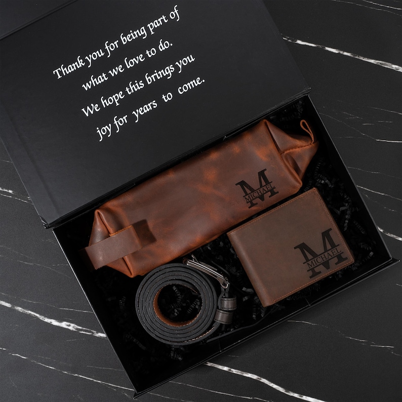 May include: A gift box containing a brown leather wallet, belt, and travel bag, all with the initial "M" and the name "MICHAEL" engraved. The box also includes a message: "Thank you for being part of what we love to do."