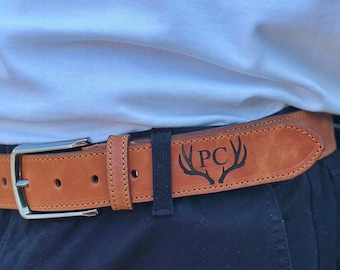 May include: A brown leather belt with a silver buckle. The belt has a deer antler design with the initials "PC" engraved on it.