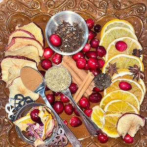 May include: A close-up of a decorative bowl filled with dried fruit, spices, and cranberries. The bowl is on a brown, ornate surface. The ingredients include dried apple slices, cinnamon sticks, cloves, star anise, and rosemary.