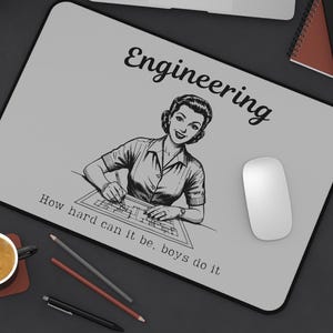 May include: A gray rectangular mousepad with the word "Engineering" and a vintage illustration of a woman drawing blueprints. The text "How hard can it be, boys do it" is also printed on the mousepad. A white computer mouse is on the right.
