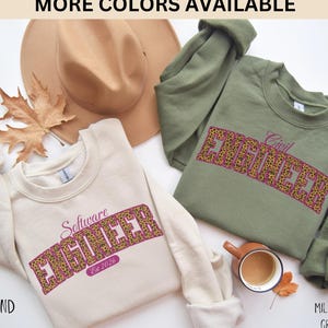 Peut inclure: Deux sweatshirts, l'un sable et l'autre vert militaire, sont présentés. Chacun porte le mot "ENGINEER" dans un motif léopard. Le sweat-shirt sable dit "Software Engineer Est 2026". Le sweat-shirt vert militaire dit "Civil Engineer".