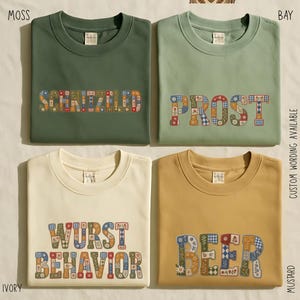 May include: Four crewneck t-shirts in moss, bay, ivory, and mustard colors. The moss shirt features the text SCHNITZLED, the bay shirt says PROST, the ivory shirt says WURST BEHAVIOR, and the mustard shirt says BEER, all in a floral patchwork pattern.