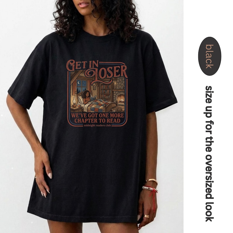 May include: Black t-shirt with a graphic that reads "Get in Loser" above an illustration of a person reading in bed. The text "We've got one more chapter to read" is below the illustration. The shirt is black.