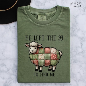 May include: Moss green t-shirt featuring the text "HE LEFT THE 99 TO FIND ME" and a cartoon sheep with a patchwork design in red, green, and white. The shirt is made of Comfort Colors material.