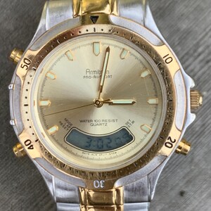 May include: A gold and silver two-tone Armitron Pro-Air Sport watch with a digital display and a gold-tone bezel. The watch face is gold with black markings and the text "Armitron Pro-Air Sport" and "Water 100 Resist Quartz".