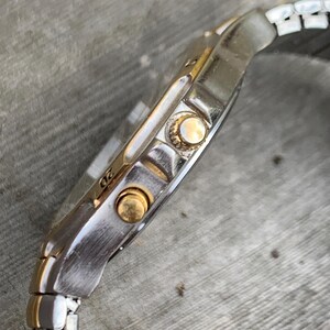May include: A silver and gold wristwatch with a metal band. The watch has a round face and three gold buttons on the side.