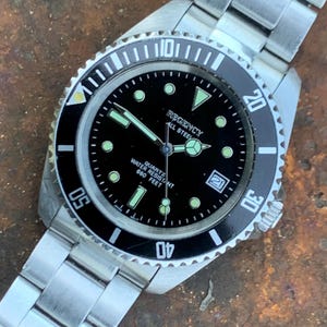 May include: A stainless steel Regency watch with a black dial and luminous hands and markers. The watch has a rotating bezel and a date window. Water resistant to 201 metres. The watch is on a stainless steel bracelet.