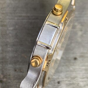 May include: A silver and gold two-tone wristwatch with a chronograph function. The watch has a round face and a silver metal band.