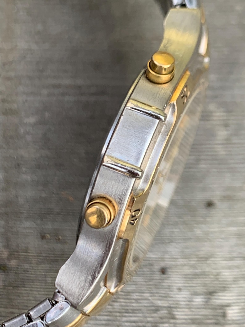 May include: A silver and gold two-tone wristwatch with a chronograph function. The watch has a round face and a silver metal band.