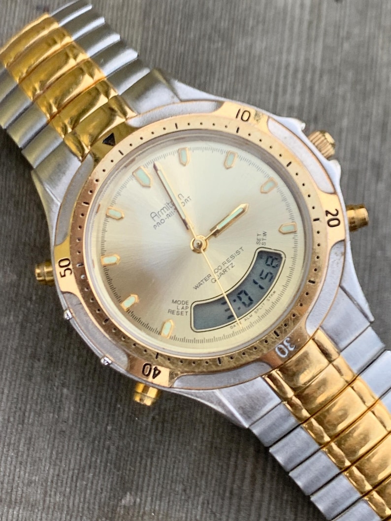 May include: A gold and silver two-tone Armitron Pro-Air-Ort watch with a white face and a digital display. The watch has a gold band and a water resistant feature.