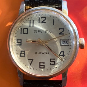 Montre Gruen Winder vintage des années 70 - 17 rubis, ton doré, cadran doré et date en bon état général - Bracelet en cuir NOS, fonctionne, donne l&#39;heure.