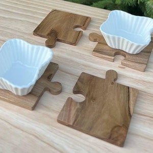May include: Four small white ceramic bowls with fluted edges sit on four wooden puzzle piece shaped coasters. The coasters are made of light brown wood.