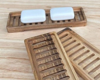 Puede incluir: Dos jaboneras de madera con fondos de listones. Los platos están apilados uno encima del otro. El plato superior tiene dos barras de jabón blancas encima.