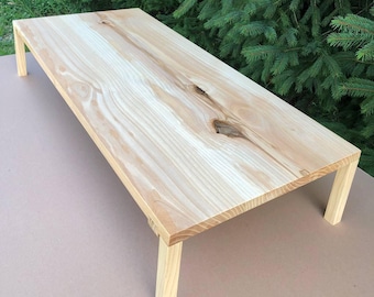 Könnte beinhalten: Ein hellfarbener Holztisch mit vier Beinen. Die rechteckige Tischplatte zeigt ein natürliches Holzmaserungsmuster mit Knoten. Der Tisch ist erhöht, was darauf hindeutet, dass es sich um einen Monitorständer oder einen kleinen Schreibtisch handeln könnte. Ca. 76 cm lang.