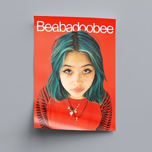 May include: A poster featuring a portrait of Beabadoobee, a singer-songwriter. The poster has a red background and features Beabadoobee with teal blue hair, wearing a red shirt with black and white stripes, and a gold necklace with a cross pendant. The text "Beabadoobee" is printed in white at the top of the poster.