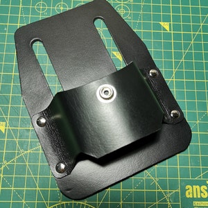 Könnte beinhalten: Schwarzer Ledergürtelholster mit einem Metall-Druckknopfverschluss. Der Holster hat eine Schlaufe zum Befestigen an einem Gürtel.