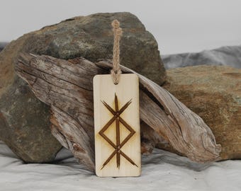 May include: A wooden pendant with a brown rope hanging from the top. The pendant is rectangular and has a wood-burned design of a Vegvisir symbol.