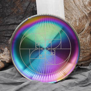 May include: A round, iridescent decorative plate with a geometric design. The plate features a spectrum of colors, including blue, green, purple, and gold. The design is a spiral pattern, with a series of lines and shapes. The plate is approximately 10 inches in diameter.