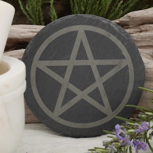 May include: A black slate coaster with a gray pentagram design. The coaster is round and has a smooth surface.
