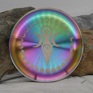 May include: A rainbow iridescent metal plate with a moon phases design and a triple goddess symbol in the center.
