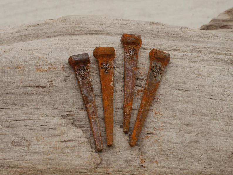 May include: Four rusty metal nails with decorative embellishments. The nails are a mix of orange and brown hues, with a weathered appearance. They are arranged on a piece of light brown wood.