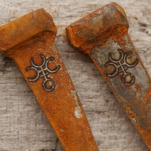 May include: Two weathered, rusty metal objects with a rectangular shape and a decorative silver design. The objects have a worn, orange-brown color, suggesting age and exposure to the elements. The design is a stylized, symmetrical pattern.
