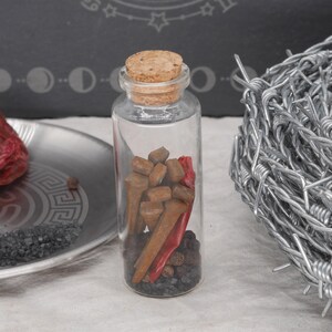 May include: A clear glass bottle with a cork stopper, filled with brown objects, red peppers, and black peppercorns. A silver plate with red peppers and black salt is to the left. A coil of barbed wire is on the right.