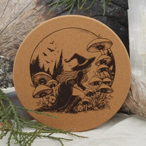 May include: Round cork coaster with a dark brown illustration of a witch in a hat, surrounded by mushrooms and a castle silhouette. The design is set against a light brown background.