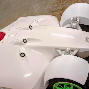 May include: A white robotic lawnmower with a red "STOP" button and green accents. The mower has a streamlined design with large wheels and a green cutting blade. The wheels have green rims and black tires.