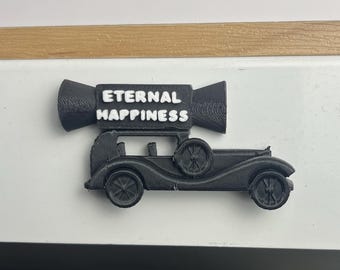 Puede incluir: Un coche negro vintage con las palabras "ETERNAL HAPPINESS" en letras blancas encima. El coche tiene cuatro ruedas y una rueda de repuesto en la parte trasera. El objeto está impreso en 3D.
