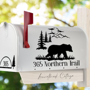 May include: White mailbox with a red flag, featuring a black silhouette design of a bear, trees, mountains, and a moon. The mailbox has the address "365 Northern Trail" and the name "Laurelbrook Cottage".