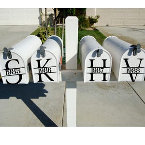 May include: Four white mailboxes with black lettering and numbers. Each mailbox has a different initial and the year 1985, 1986, 1987, and 1988. The mailboxes are mounted on a white wooden post.