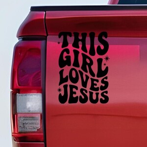 Peut inclure: Autocollant en vinyle noir avec le texte "THIS GIRL LOVES JESUS" dans une police rétro, apposé sur un véhicule rouge. L'autocollant comprend des étoiles.