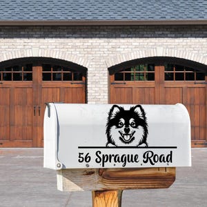 May include: A white mailbox with a black and white Pomeranian dog graphic and the address "56 Sprague Road" in black text. The mailbox is mounted on a wooden post in front of a brick house with wooden garage doors.