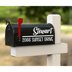 May include: A black metal mailbox mounted on a white wooden post. The mailbox features white vinyl lettering that reads Stewart above a horizontal line, with 2066 SUNSET DRIVE printed below. A bright red metal signal flag is attached to the side.