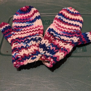 Może przedstawiać: Para dzianych rękawiczek w paski w kolorze różowym, białym, niebieskim i ciemnoniebieskim.