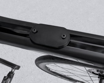 May include: Close-up of a black bicycle frame with a black, oval-shaped cover secured by two screws. The image shows a portion of the wheel and the frame's sleek design, suggesting a focus on cycling components and accessories.