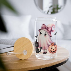 May include: A clear glass can-shaped tumbler with a bamboo lid and straw. The tumbler features a Halloween-themed illustration of a ghost wearing a pink witch hat, holding a pumpkin, and accompanied by a black cat and bats.