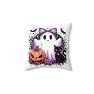 May include: White square pillow with a Halloween-themed design. Features a cartoon ghost with a purple bow, a jack-o'-lantern, and a black cat. The design includes bats and purple floral accents.