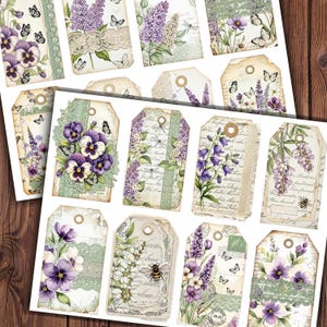 Puede incluir: Un conjunto de etiquetas de regalo de estilo vintage con diseños florales. Las etiquetas presentan pensamientos morados, lavanda y otras flores, acentuadas con mariposas, encaje y escritura. Las etiquetas tienen un aspecto envejecido, con un agujero para ensartar.