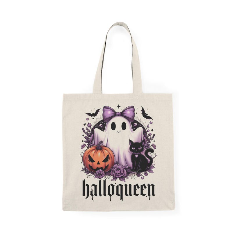 May include: A beige tote bag featuring a Halloween-themed design. The graphic includes a ghost with a purple bow, a jack-o'-lantern, and a black cat. The word "halloqueen" is printed in a gothic font below the image.