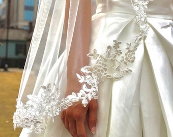 May include: A white bridal veil with delicate lace trim. The veil is made of soft tulle and features a floral design.