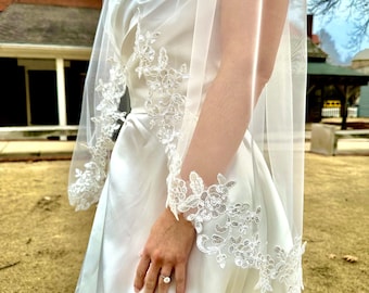 May include: A white wedding dress with a lace trim and a veil. The dress has a sweetheart neckline and a fitted bodice. The veil is made of tulle and has a lace trim.